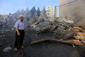 Fire is seen as a Palestinian man walks amidst the remains of a tower building housing offices, which witnesses said was destroyed by an Israeli air strike, in Gaza City August 26, 2014. Israeli air strikes launched before dawn on Tuesday killed two Palestinians and destroyed much of one of Gaza's tallest apartment and office buildings, setting off huge explosions and wounding 20 people, Palestinian health officials said. Israel had no immediate comment on the attacks that took place as Egyptian mediators stepped up efforts to achieve an elusive ceasefire to end seven weeks of fighting. Israel launched an offensive on July 8, with the declared aim of ending rocket fire into its territory. Photo by Mohammed Asad
